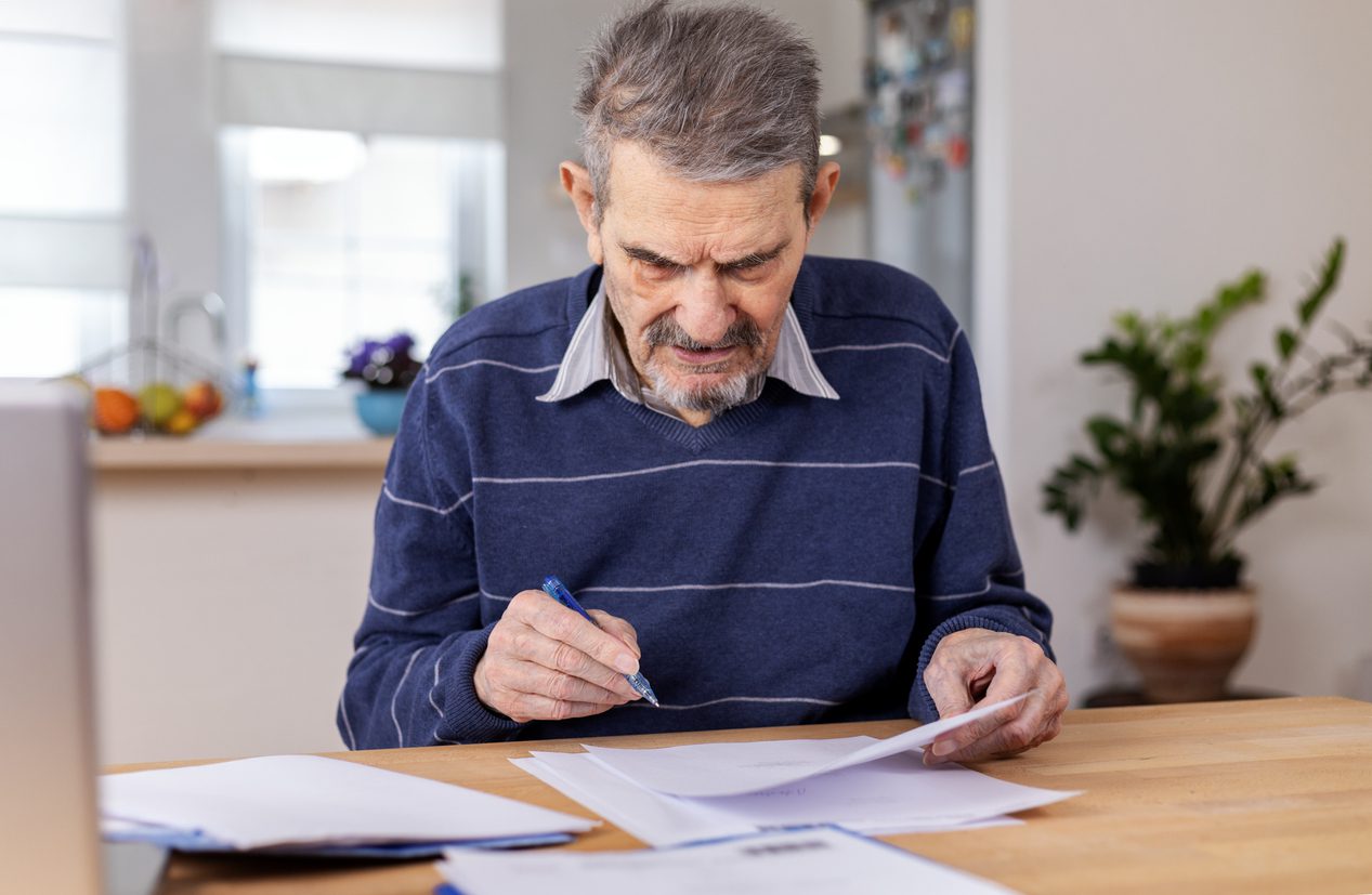 Senior man reviewing documents, potentially social security benefit documentation, with frustration