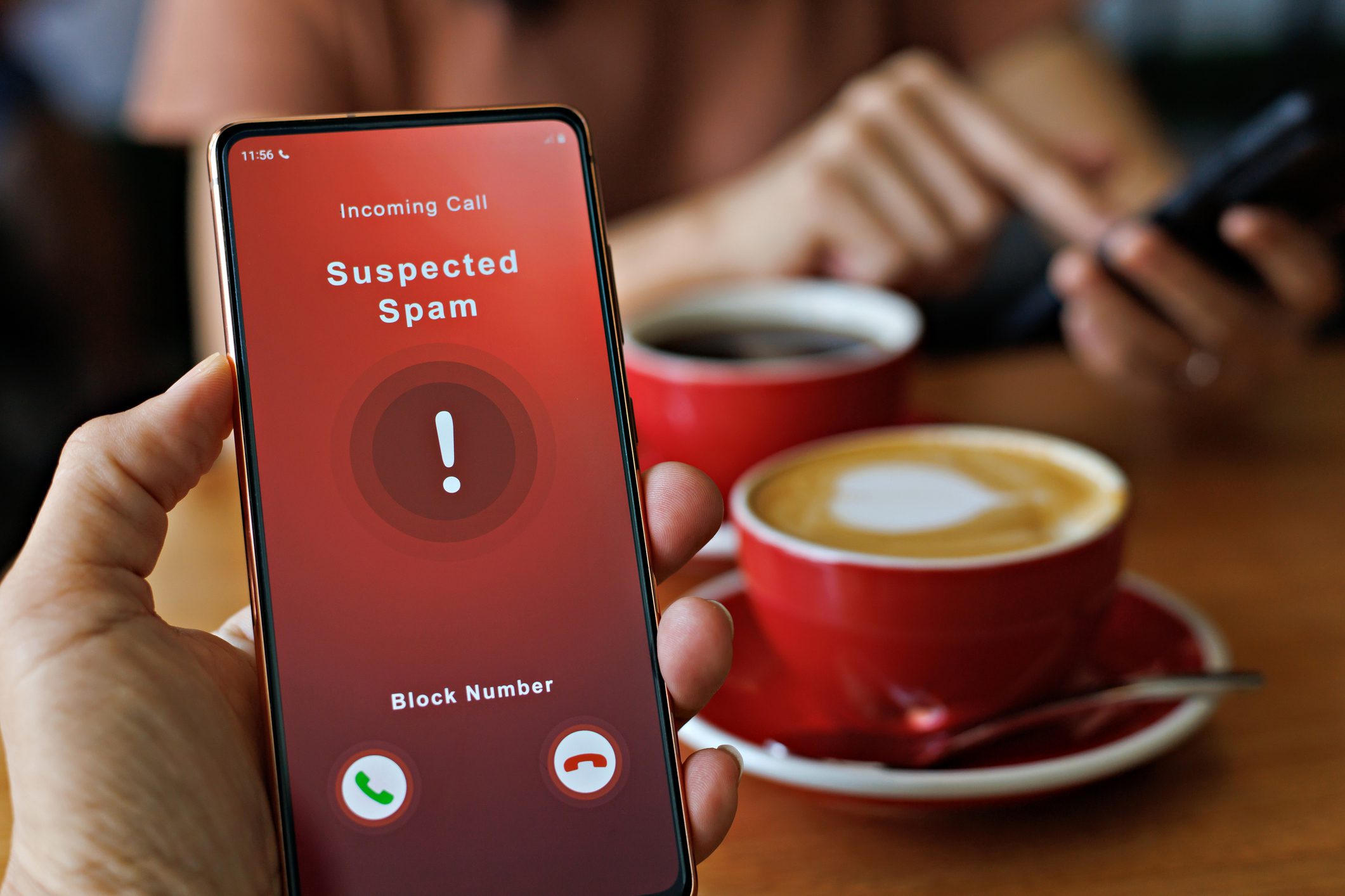 Spam call appearing on phone screen while two people enjoy coffee.