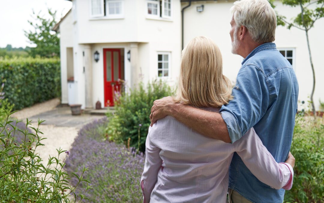 Rear View Of Mature Couple Standing In Garden Look At Dream Home In Countryside