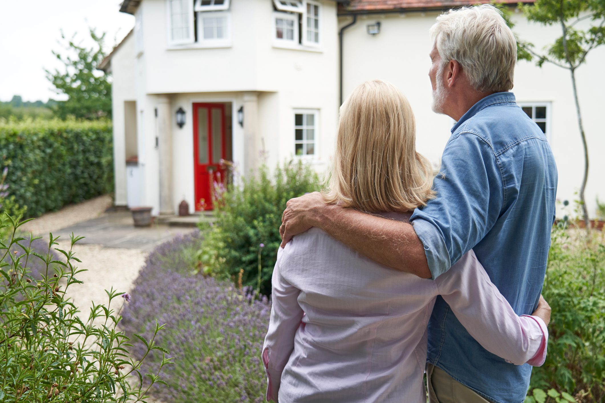 Rear View Of Mature Couple Standing In Garden Look At Dream Home In Countryside Rear View Of Mature Couple Standing In Garden Look At Dream Home In Countryside