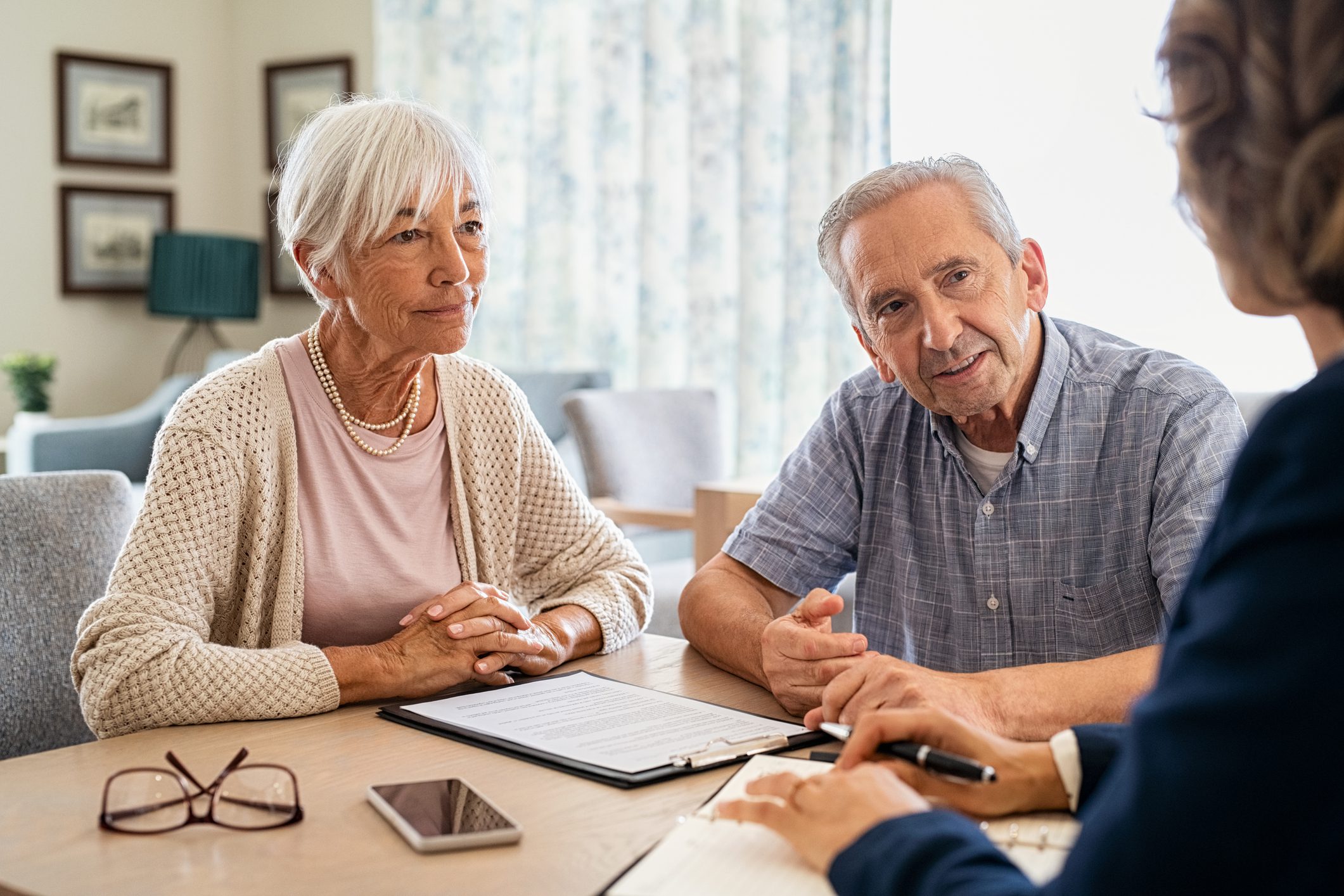 Senior couple planning their investments with financial advisor Senior man and woman meeting medical adviser for health insurance at home. Old couple planning their investments with financial advisor after retirement at home. Aged couple consulting with insurance agent while sitting together with prospectus at home.