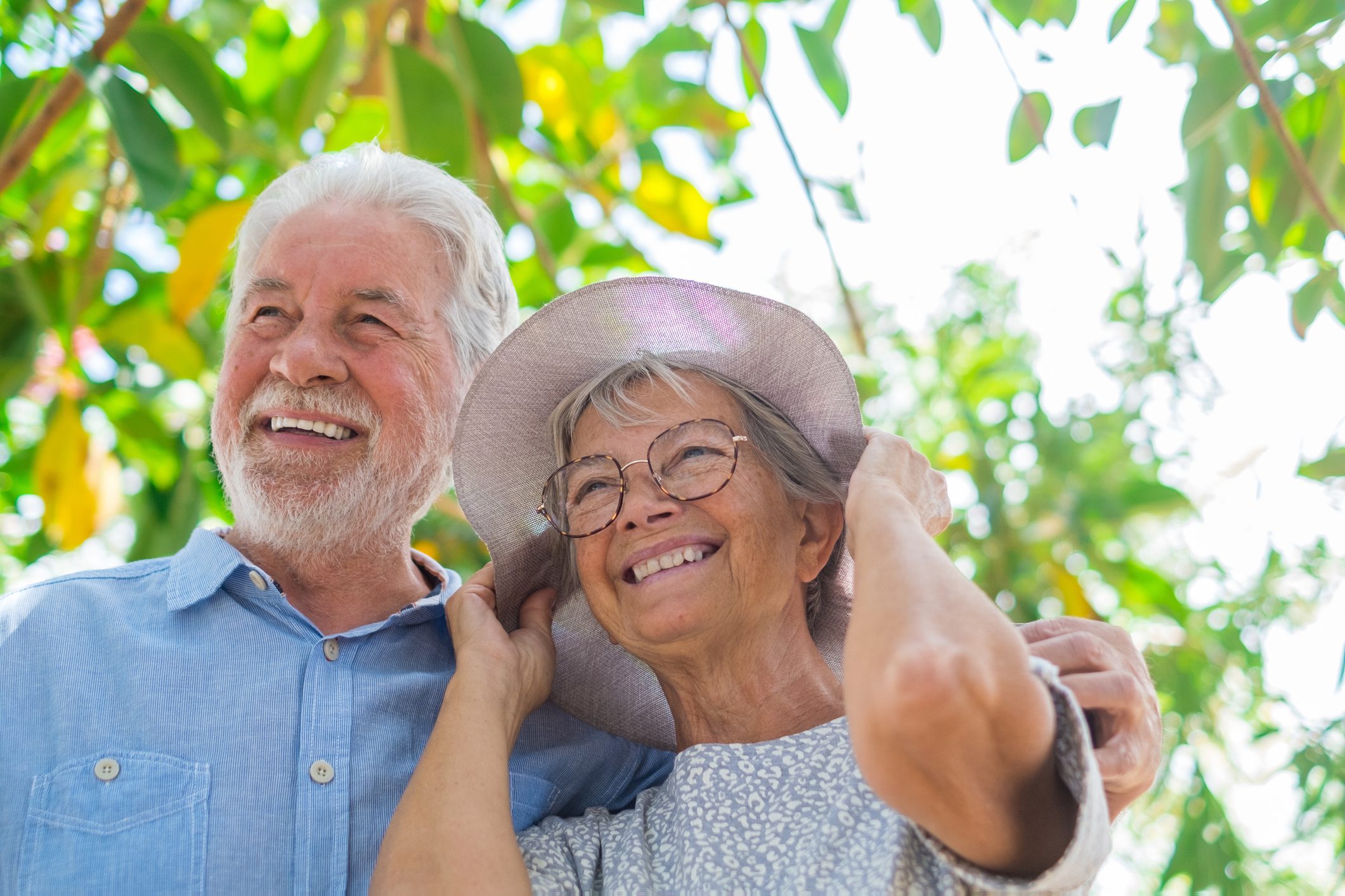 Elderly couple embracing in spring park outdoors having fun and enjoying together looking at the trees. Two old and mature people in love caring each other.