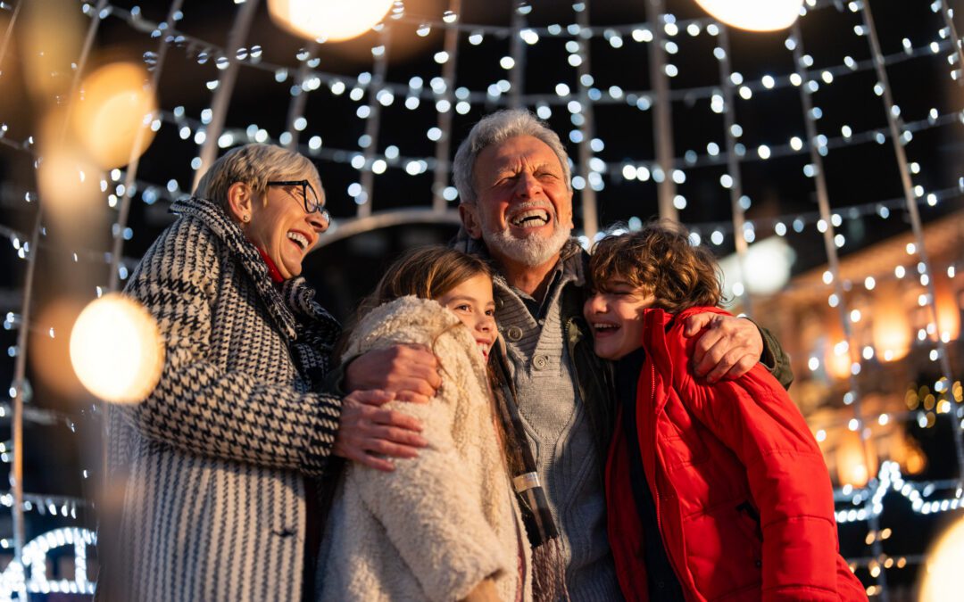 Overjoyed senior couple having fun with granddaughter and grandson surrounded with Christmas lights during winter holidays.