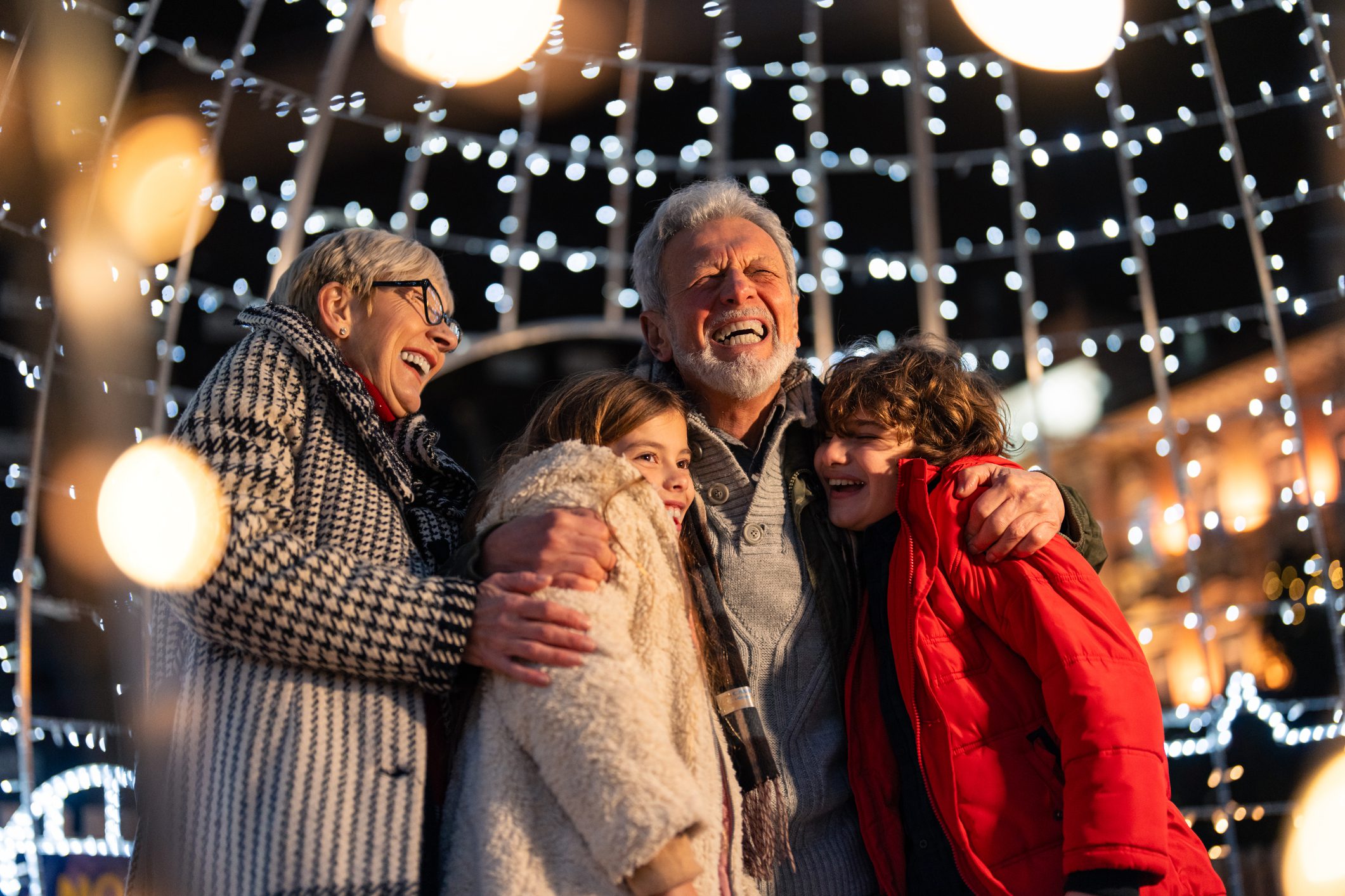 Overjoyed senior couple having fun with granddaughter and grandson during winter holidays Overjoyed senior couple having fun with granddaughter and grandson surrounded with Christmas lights during winter holidays.