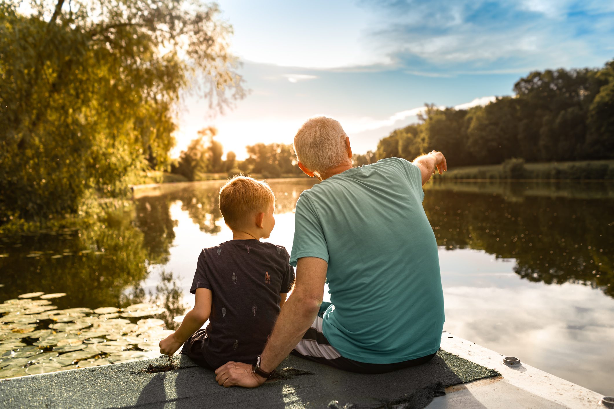 Young boy and his grandfather spending time at the park forest lake.