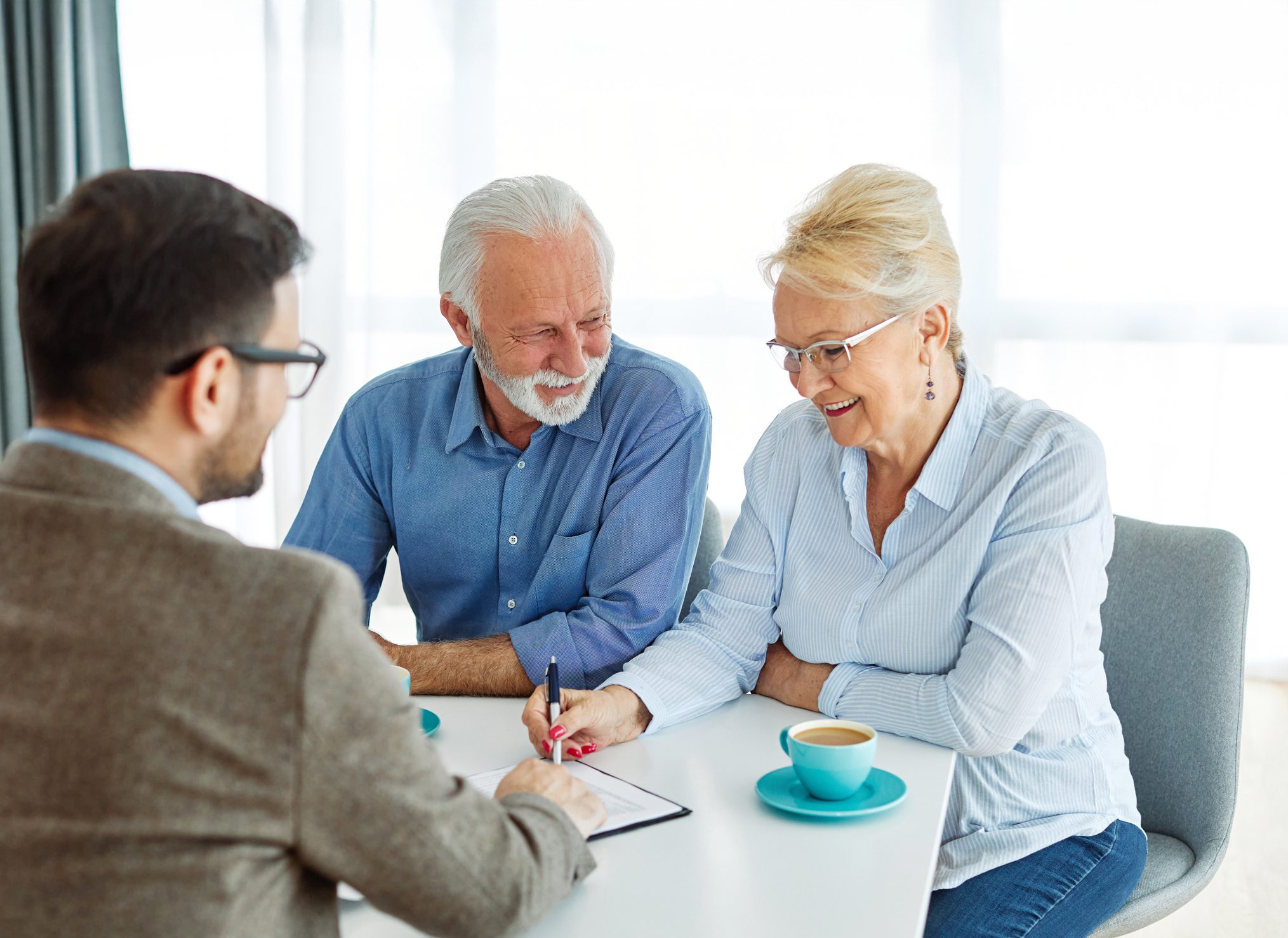 Portrait of a businessman or real estate agent or doctor shaking hands and signing a deal contract  with senior couple in his office