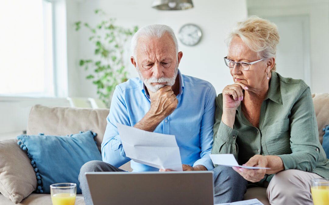 Senior couple checking bills and calculating expenses using a laptop at home, debt taxes concept, worried married elderly couple