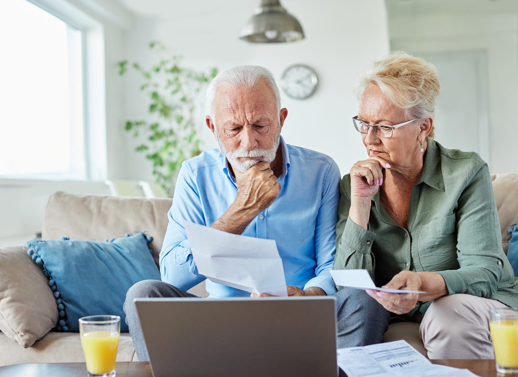 Senior couple checking bills and calculating expenses using a laptop at home, debt taxes concept, worried married elderly couple