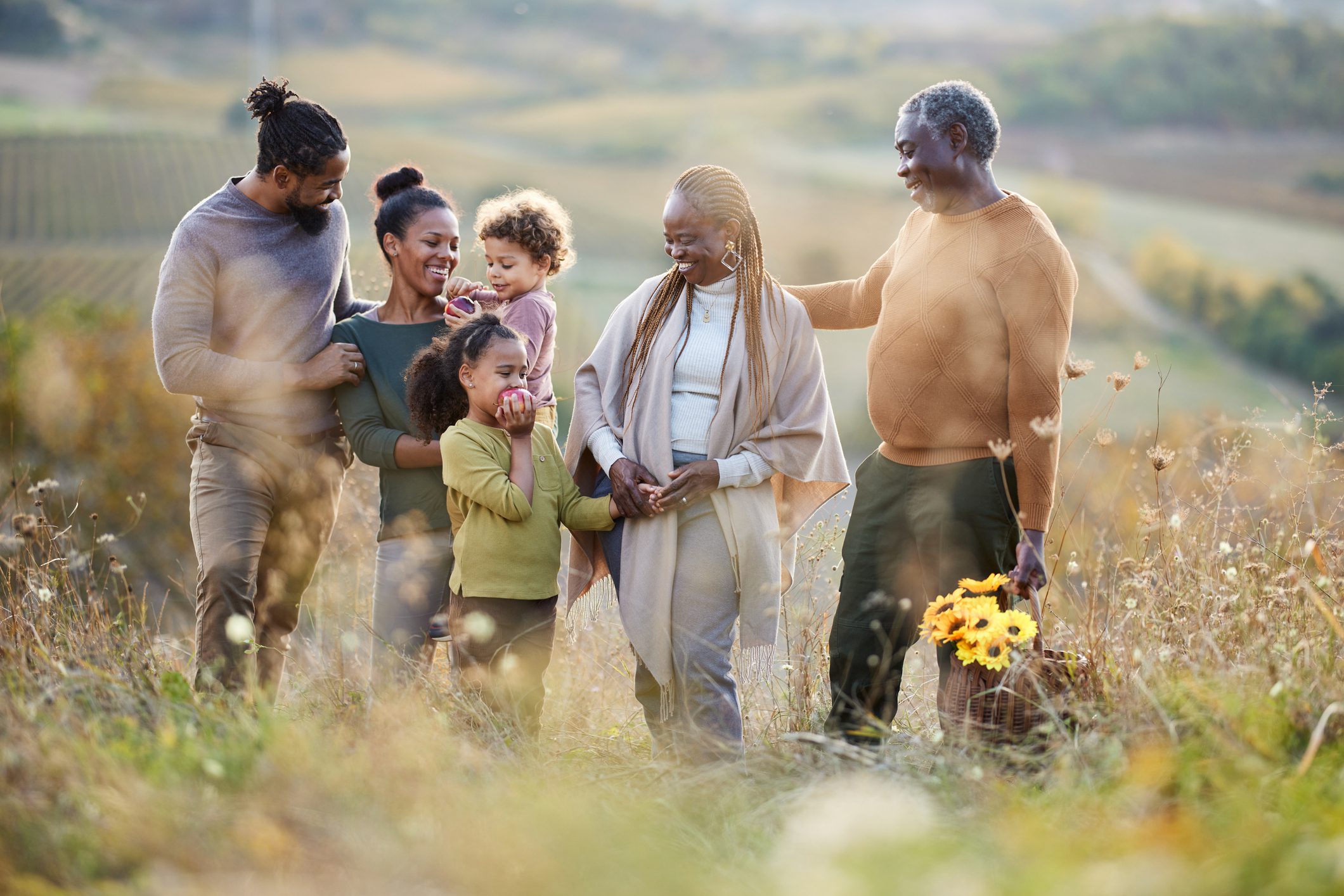 Happy African American multi-generation family communicating while going on a picnic during autumn day on a hill.