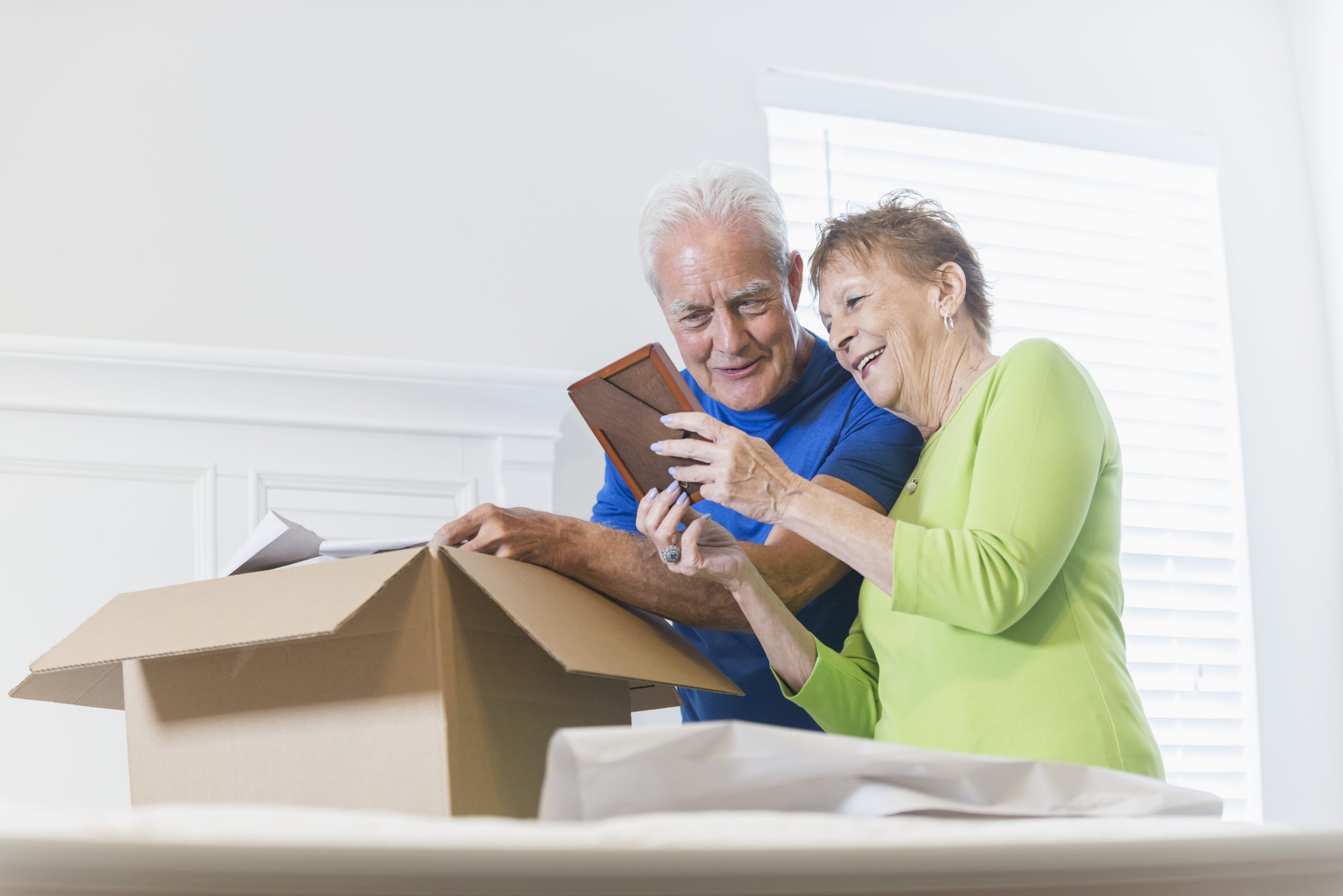 Senior couple packing box, looking at picture frame A senior couple moving house, packing a cardboard box in the bedroom. They are talking and smiling, looking at a picture frame which is bringing back memories.
